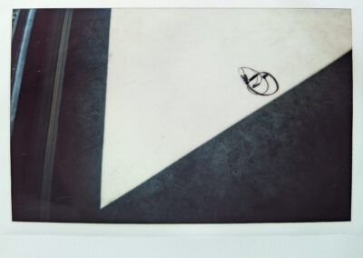 Wide format polaroid photograph of a pair of wired earphones coiled on a pale surface, bisected by a sharp diagonal shadow from a window frame.